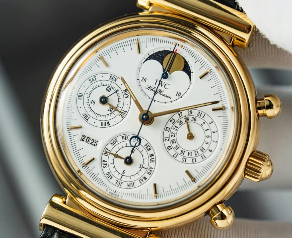 Närbild av exklusivt armbandsur i guld med vit urtavla, flera komplikationer och tydliga visare. Klockan har månfasvisning, kalenderfunktioner och detaljrik design som speglar hög hantverkskvalitet och klassisk urmakarkonst.